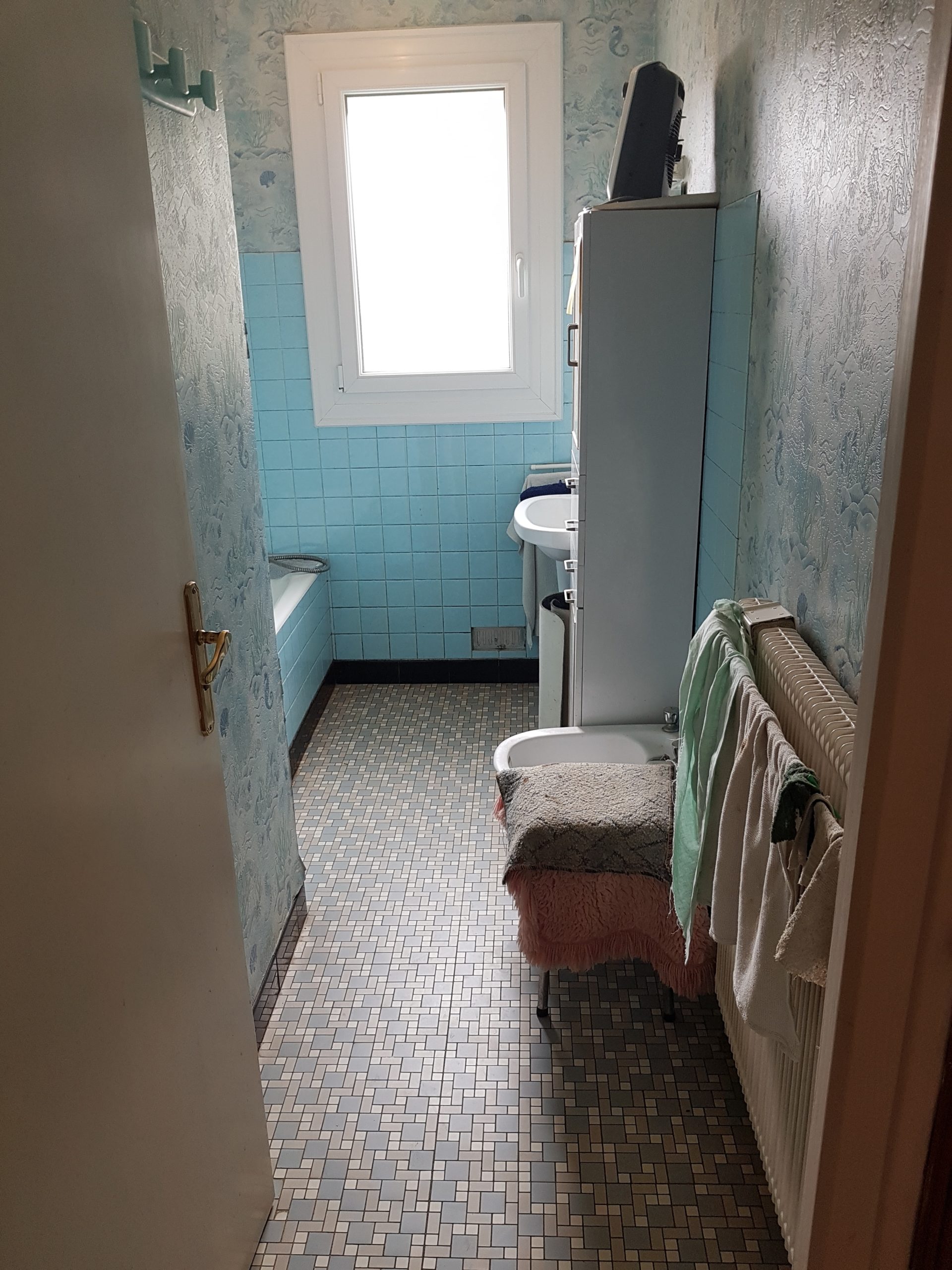 Photo d'une salle de bain avant rénovation avec de la faïence bleue, un lave main et une baignoire