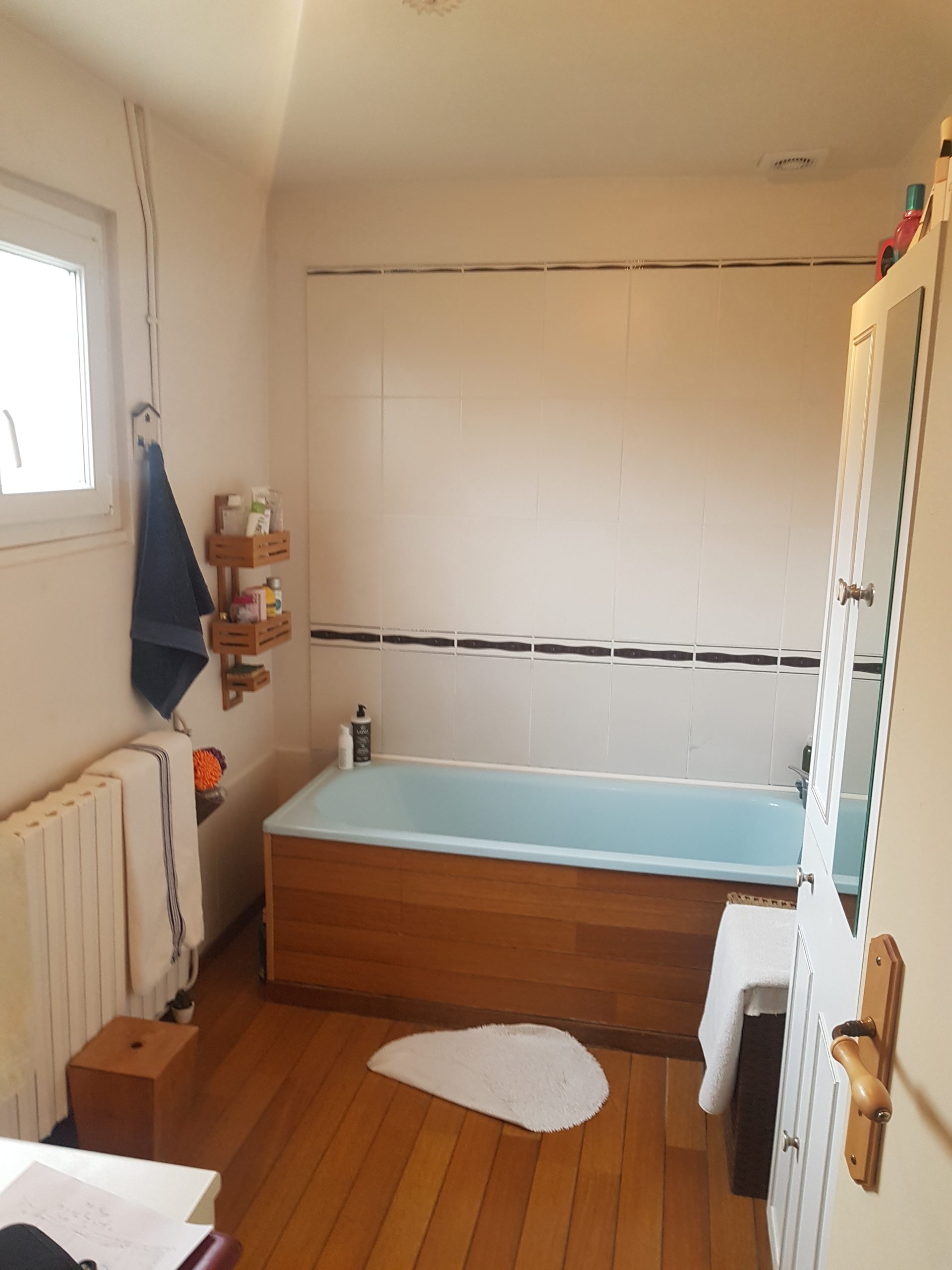 Photo d'une salle de bain avant rénovation avec une baignoire posée sur du parquet et des murs blancs